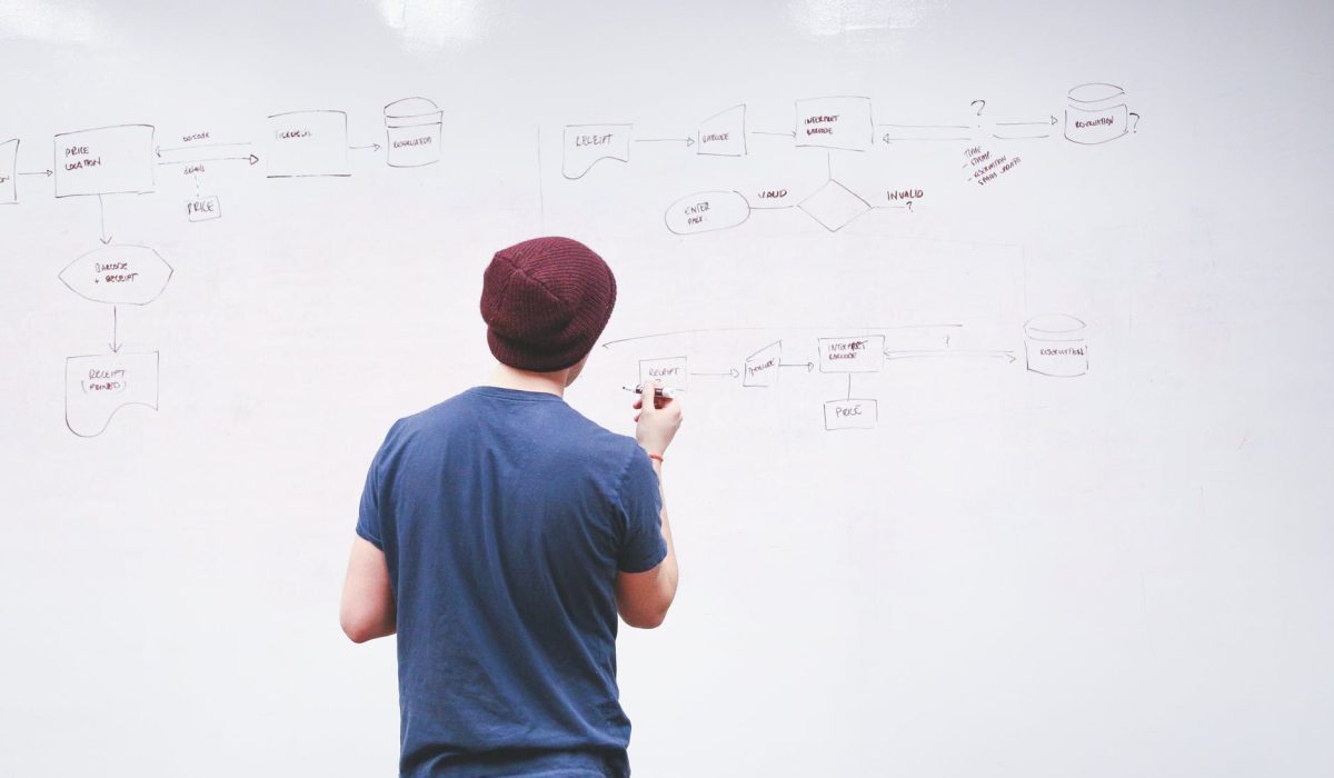 man standing while holding red marker pen facing marker board